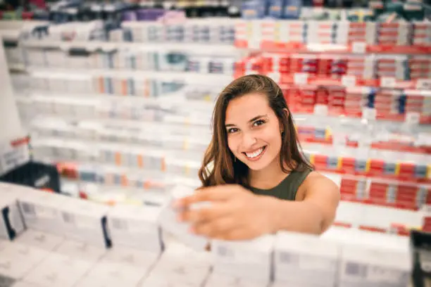 Young woman holding cosmetics in her hand in supermarket.