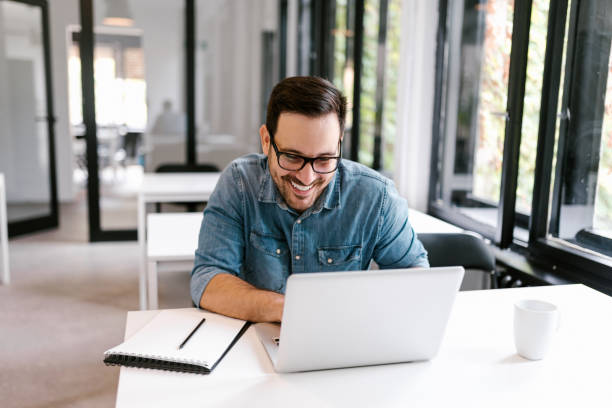 istock Cheerful businessman using laptop in bright office space. 1022992914