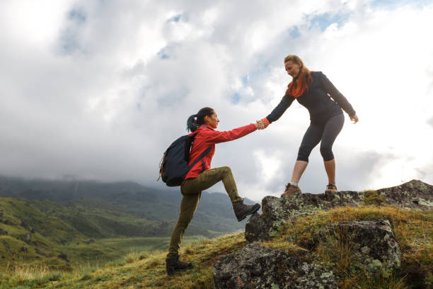 Girls helping each other hike up a mountain at sunrise. Giving a helping hand, and active fit lifestyle concept. stock photo