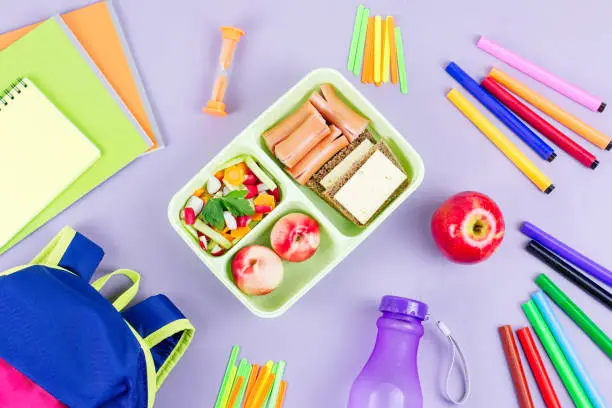 School concept flat lay. Kid backpack, lunchbox, water bottle, notebook, markers on wooden desktop, top view