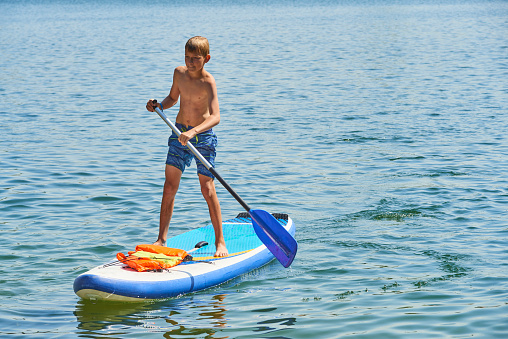 Paddle boarder. Child boy paddling on stand up paddleboard. Healthy lifestyle. Water sport, SUP surfing tour in adventure camp on active family summer beach vacation.