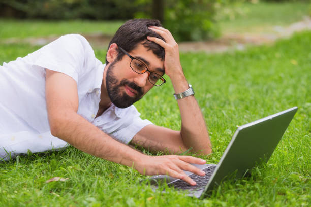 istock Young man working on his laptop while lying on the grass of the park. bored expression. 1023038634