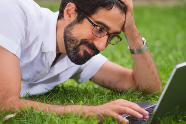istock Young man working on his laptop while lying on the grass of the park. Happy expression, concept of freedom. 1023038780