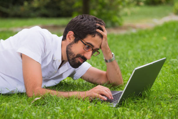 istock Young man working on his laptop while lying on the grass of the park. Happy expression, concept of freedom. 1023038830