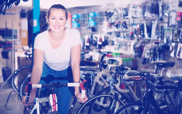Portrait of  cheerful positive  woman who is standing with new bicycle indoors.