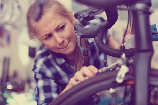 Young  positive  woman master is repairing bicycle in workshop.