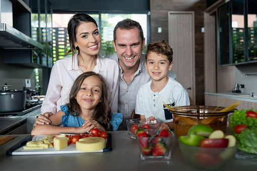 Beautiful portrait of family in the kitchen preparing dinner while looking at camera smiling very happy