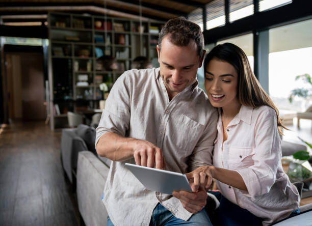 istock Man pointing something on tablet to his partner while sitting on couch at their apartment 1023053254