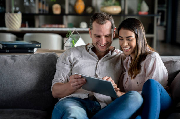 istock Happy couple at home relaxing on couch while looking at photos on tablet 1023053288