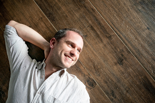Happy man relaxing on a wooden floor daydreaming and smiling