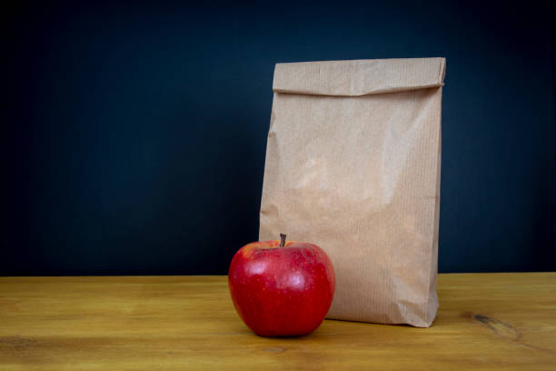 学校給食。茶色の紙袋や木製の机の上に赤いリンゴ - packed lunch paper bag apple lunch ストックフォトと画像