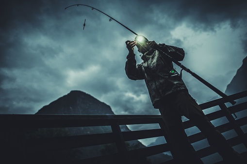 Fly Fishing at Night. Caucasian Fisherman on the Wooden Marina Deck in the Fjord.