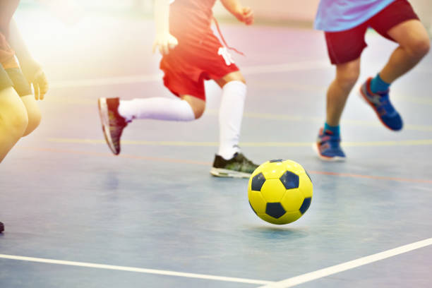 Children playing soccer with yellow football indoors