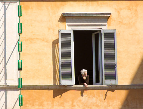 Rome, Italy: Senior woman leaning out of sunny window in the Trastevere neighborhood of Rome.