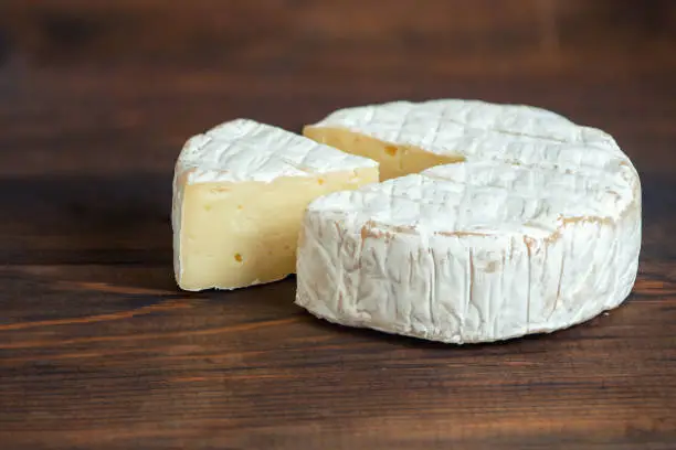 A soft ripened Camembert cheese on dark wooden board.