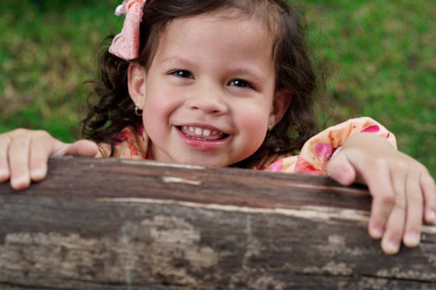 Family playing in the park Beautiful latin girl between 3 and 5 years old, with beautiful and expressive eyes, who smiles at the camera, hidden behind the branch of a tree niñas stock pictures, royalty-free photos & images