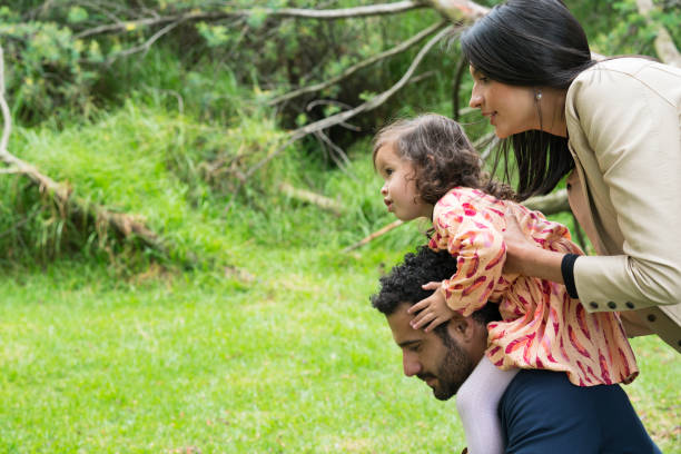 Family playing in the park Family, Latina, with their parents between 25 and 30 years old and a little girl between 3 and 5 years old, playing happily, while the Pope holds the little girl on her shoulders niñas stock pictures, royalty-free photos & images