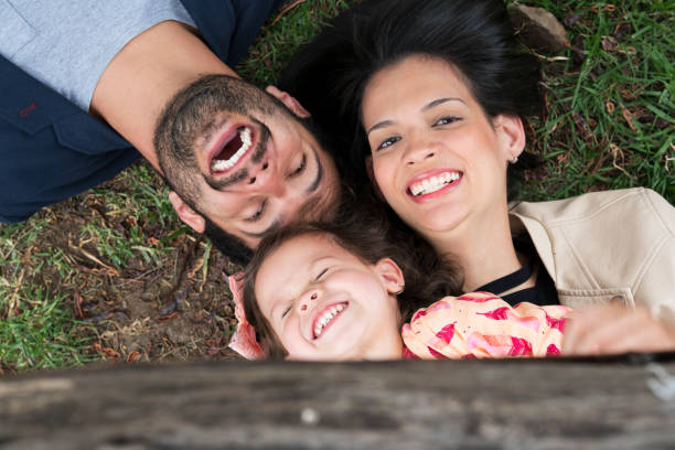 Family playing in the park Family of young Latinos between 25 and 30 years old, with a small girl between 3 and 5 years old, sitting on the lawn smiling as they look at the sky niñas stock pictures, royalty-free photos & images