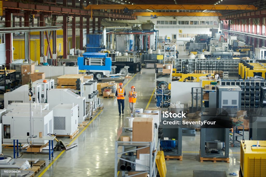 Inspection in Plant Workshop High angle full length portrait of bearded businessman wearing hardhat walking across production workshop accompanied by female factory employee, copy space Factory Stock Photo