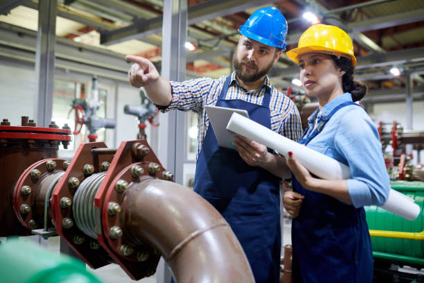 Workers in Water Purification System Portrait of two factory workers pointing away while working with piping and machines in modern workshop, copy space basic industry stock pictures, royalty-free photos & images