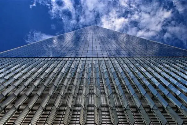 New York City's new One World Trade Center disappears into the deep blue sky and white clouds reflected in its windows.