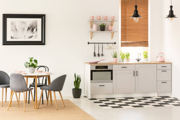 istock Real photo of open space kitchen interior with dining table with chairs, window with wooden blinds and pink accessories on countertop 1023182486