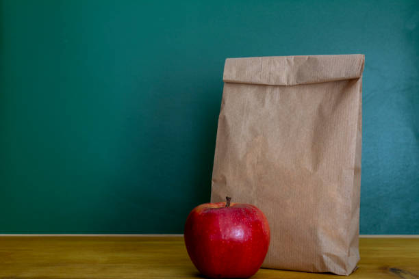 学校給食。茶色の紙袋や木製の机の上に赤いリンゴ - packed lunch paper bag apple lunch ストックフォトと画像