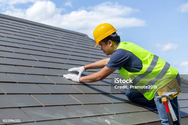 屋根の修理白い手袋グレーのタイルや家の鉄片青空背景とコピー スペースで置き換えるとワーカー屋根ふき 建設労働者がそれをカバーするタイルで屋根の上に立っています - 屋根のストックフォトや画像を多数ご用意