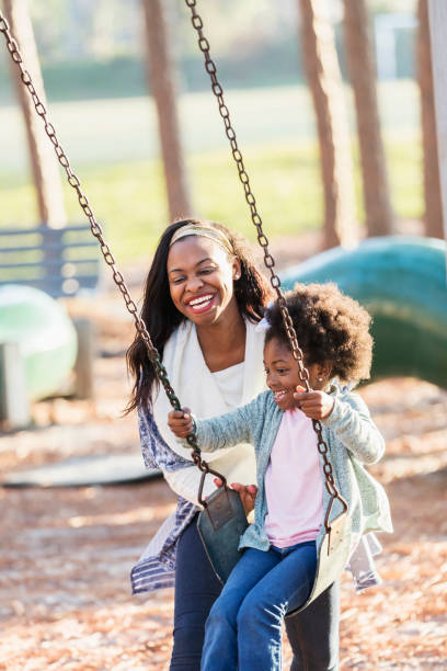 afroamerykańska dziewczyna z matką na placu zabaw na huśtawce - child swinging playground african descent zdjęcia i obrazy z banku zdjęć