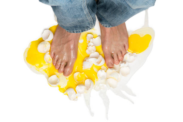 Walking on Eggshells This is an overhead photograph of a barefoot man walking on broken eggs shells with the yoke spilling out isolated on a white background. animal egg walking on eggshells walking broken stock pictures, royalty-free photos & images