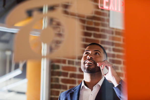 Businessman in booth talking on mobile phone A mid adult mixed race Hispanic and African-American man in his 30s with short hair, a beard and mustache, talking on his mobile phone, in a designated area for making telephone calls. pay phone on the phone latin american and hispanic ethnicity talking stock pictures, royalty-free photos & images