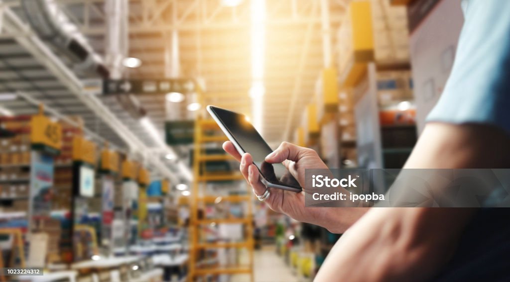 Factory worker using application on mobile smartphone to operate automation for modern trade. Checking order in large warehouse. Import and export the shipping cargo. Mobile Phone Stock Photo