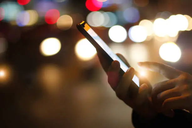 Close up female hands using mobile smartphone in illuminated color light bokeh on street night background