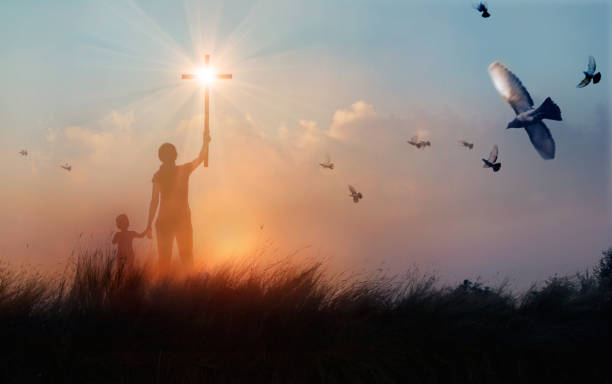 日没の背景、崇拝の概念にイエス様に祈りながらクロスを上げる母と息子のキリスト教の祈りのシルエット。 - cross sunset sky spirituality ストックフォトと画像
