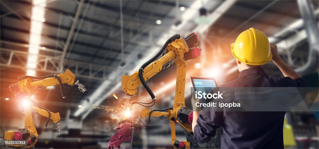 Ingeniero utilizando tablet y controlar automatización robot brazos máquina en fábrica inteligente industrial sobre el control de software del sistema. Soldadura robótica y operación de fabricación digital. - Foto de stock de Industria libre de derechos