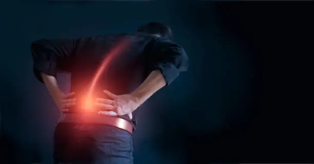 Photo of Man suffering from back pain cause of office syndrome, his hands touching on lower back. Medical and heath care concept