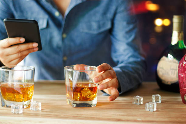 istock Man using smartphone while drinking of whiskey alcoholic beverage at bar counter in the pub. 1023248296