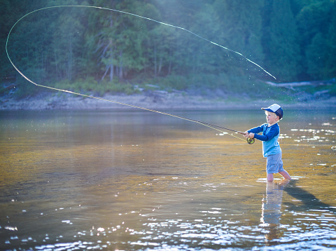 A young boy casting a fly rod at a wilderness lake.