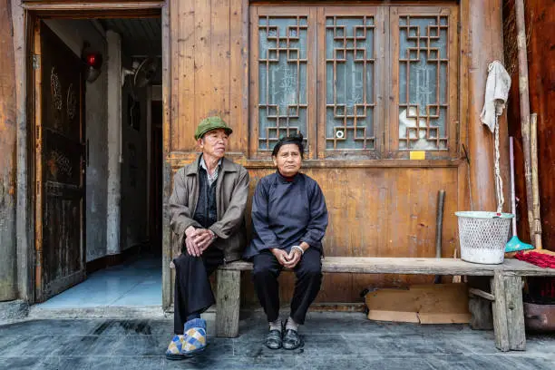 Chinese senior couple sitting side by side on a bench in front of their home in a rural chinese village. Chinese Real People Portrait. Zhaoxing, Guizhou, China