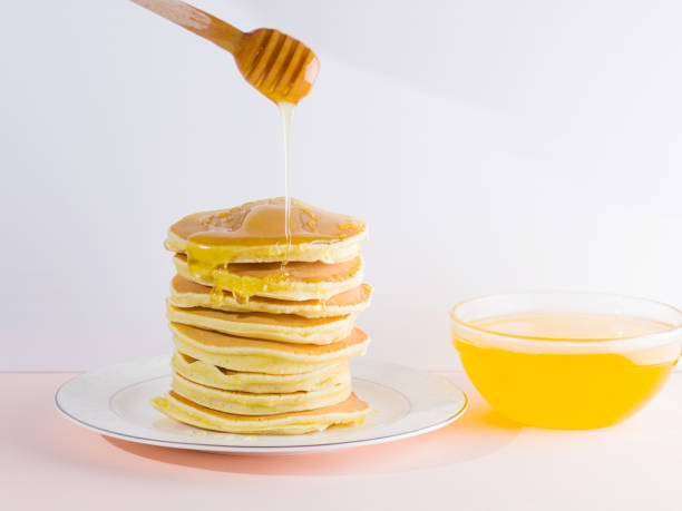 istock Pancakes on a white pink background. Hot pancakes with honey on a white plate with copy space. Delicious dish for breakfast in the style of pop art. Honey flows down from a wooden stick on a dish 1023346744