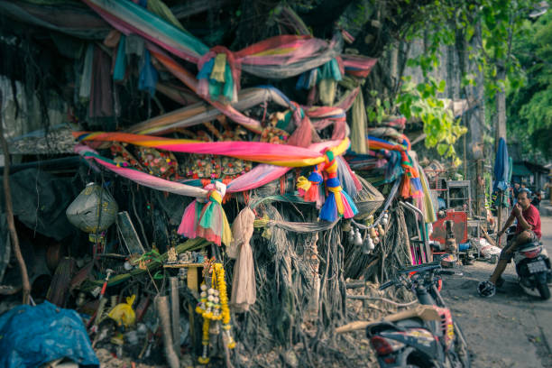 Bangkok, Thailand - May 02 2018:  Numerous colourful ribbons are tied around this sacred fig tree (Ficus Religiosa).  Also known as Bodhi tree or Banyan tree.  Buddha was said to have sat under such a tree when he received enlightenment.  Animists also believe that spirits dwell in these trees.  Ribbons are tied to appease the spirits and protect the trees.  The practise is widespread in Thailand.  The location here is downtown Bangkok.