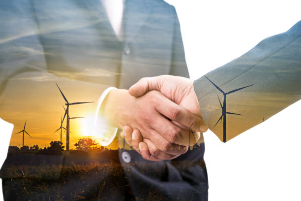 Double exposure of business handshake partnership with wind turbine farm plant background stock photo