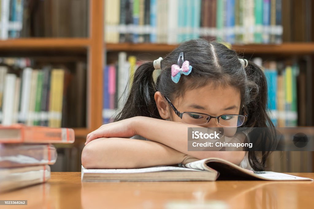 Unsuccessful educational system concept with Asian child girl student getting bored reading book in school classroom library Child Stock Photo