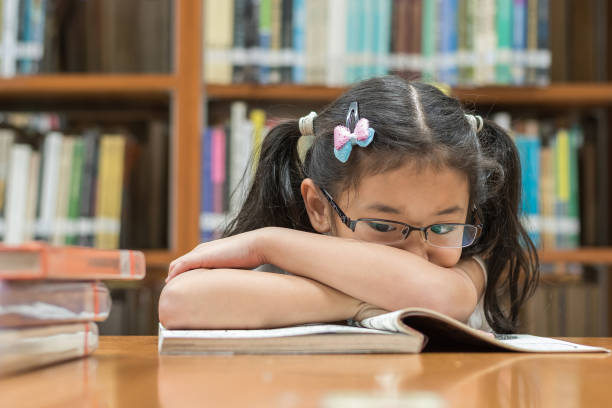 nieudana koncepcja systemu edukacyjnego z azjatyckim dzieckiem dziewczyna student coraz nudzi czytanie książki w bibliotece szkolnej - mathematics elementary student child student zdjęcia i obrazy z banku zdjęć