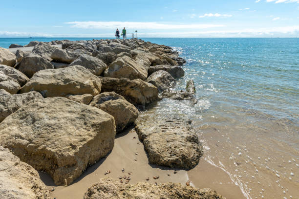 Rocky sea defence in Sandbanks, Poole Poole, UK - August 21 2018: A man and woman stand on the rocky sea defence at Sandbanks in Poole on a sunny day. sandbanks poole harbour stock pictures, royalty-free photos & images