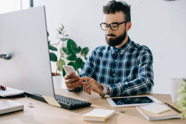 istock handsome bearded young businessman using smartphone at workplace 1023378752