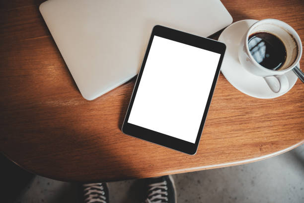 istock Top view mockup image of a black tablet pc with blank desktop white screen with laptop and coffee cup on wooden table 1023384826