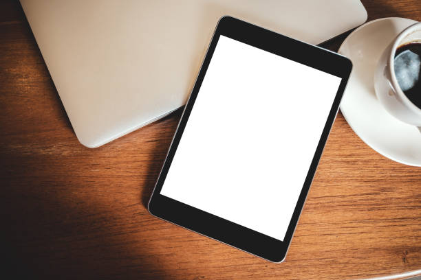 istock Top view mockup image of a black tablet pc with blank desktop white screen with laptop and coffee cup on wooden table 1023384848