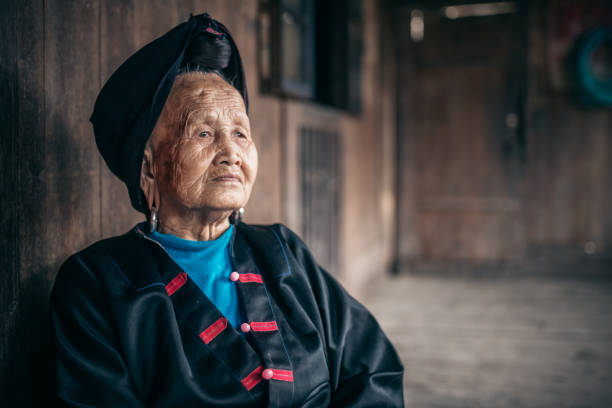 old pensive chinese minority woman sitting in old wooden house