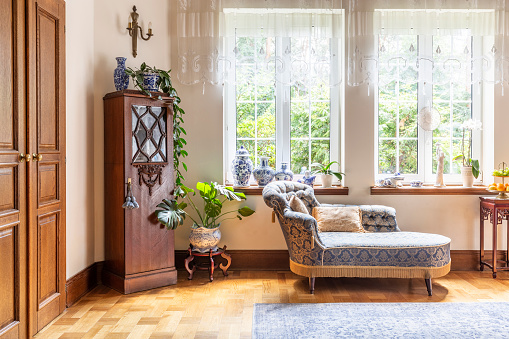 Un interior lujoso salón con un sofá y una madera gabinete sobre un parquet contra dos grandes ventanas. Foto real. photo